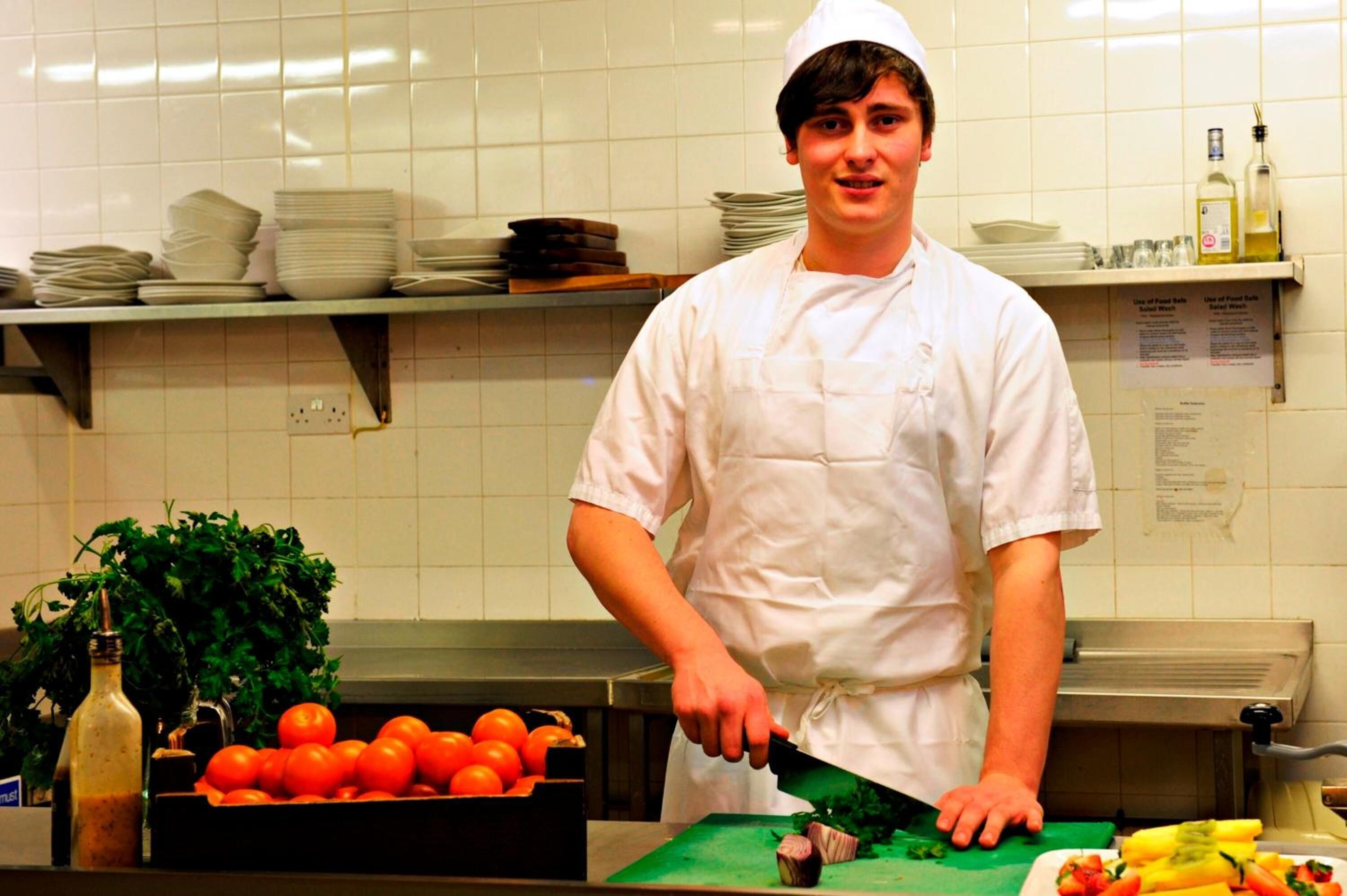 Um chef em cozinha com tábua de corte, tomates e faca.