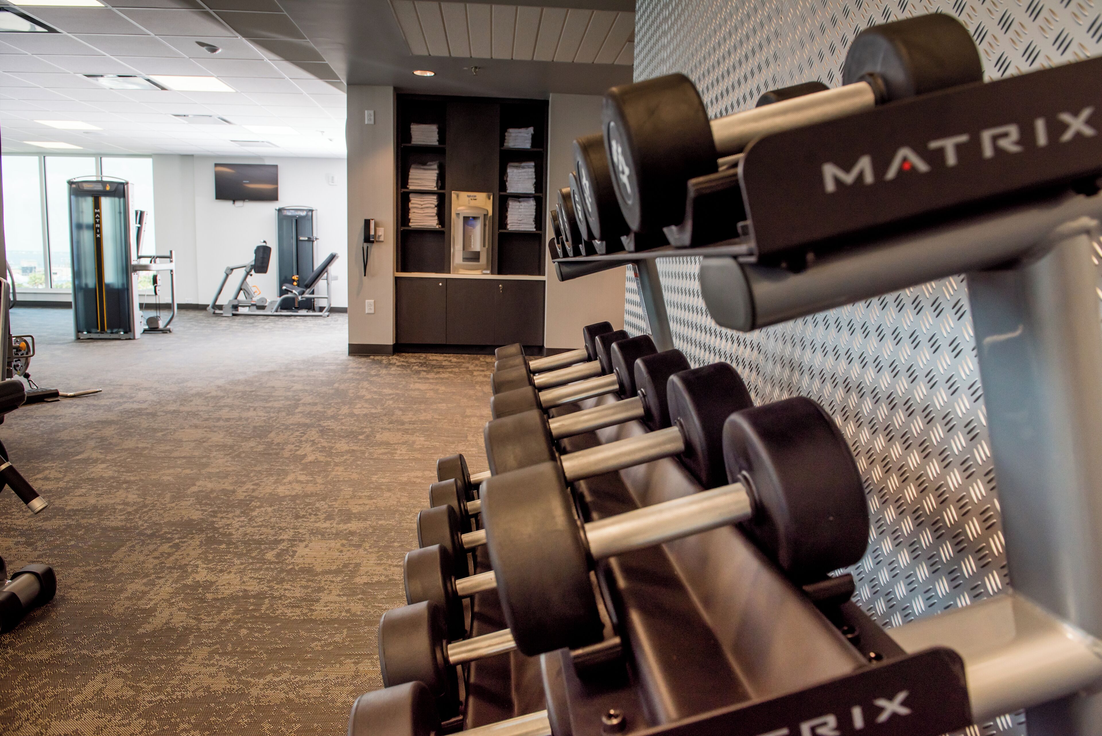 A gym with a row of MATRIX branded dumbbells, a treadmill, and a water dispenser in the background.
