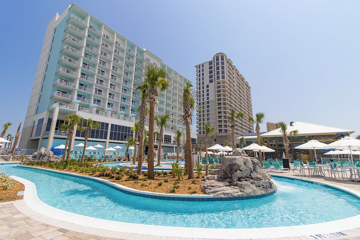 Un hotel con piscina, palmeras y un edificio grande con balcones.