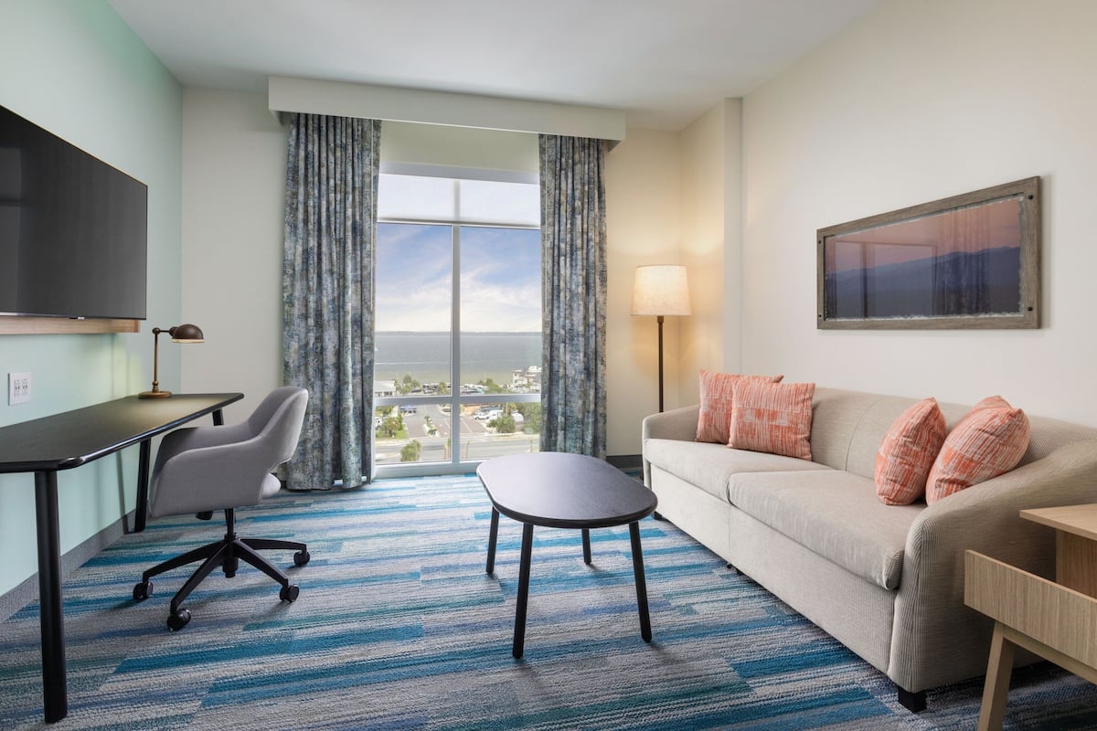 Ein Hotelzimmer mit Schreibtisch, Bürostuhl, Sofa und Blick auf die Stadt durch große Fenster.