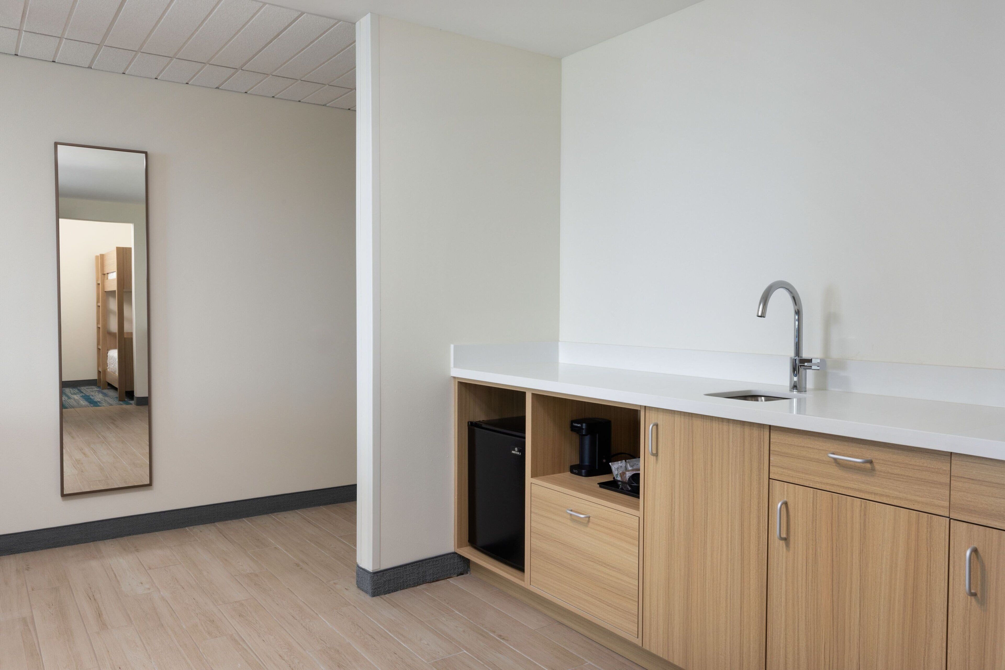 A modern bathroom with a white countertop, a sink, a mirror, and wooden cabinets.