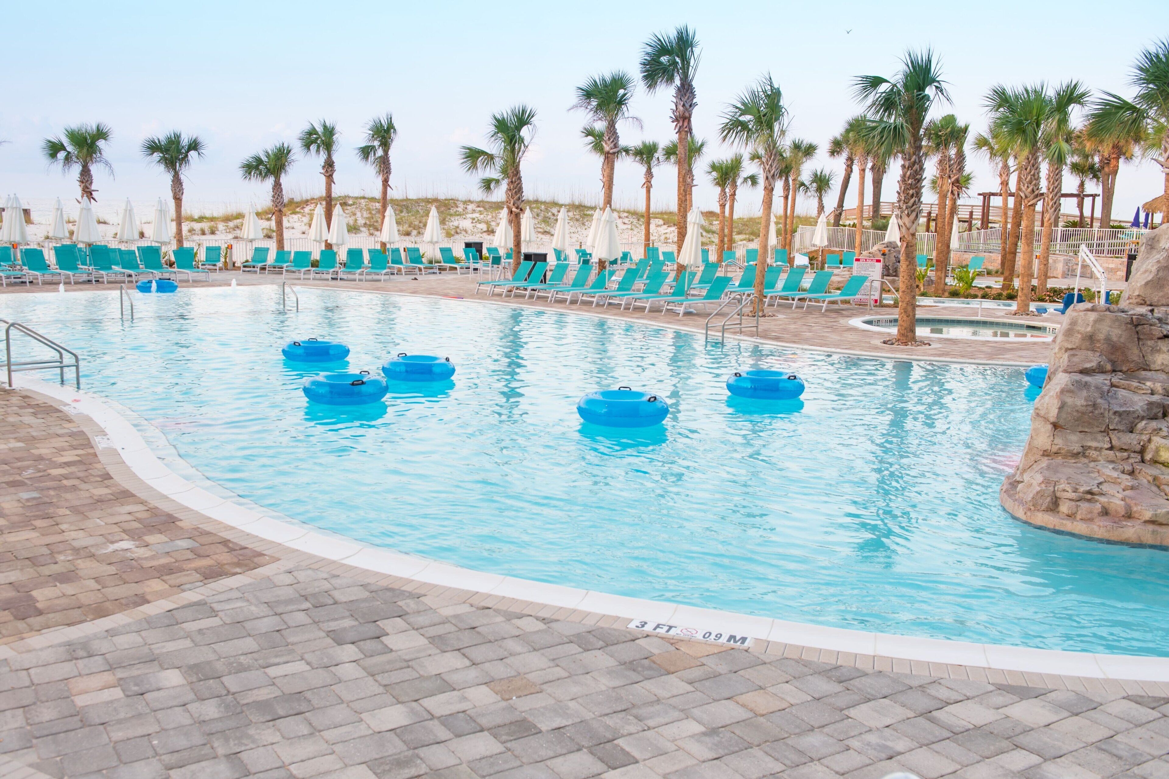 Una piscina con acqua blu, circondata da palme e comode sedie a sdraio.