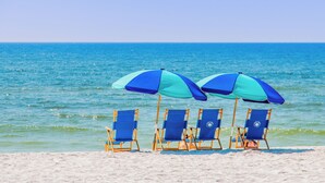 Een strand met vier blauwe en turquoise strandstoelen en parasols.