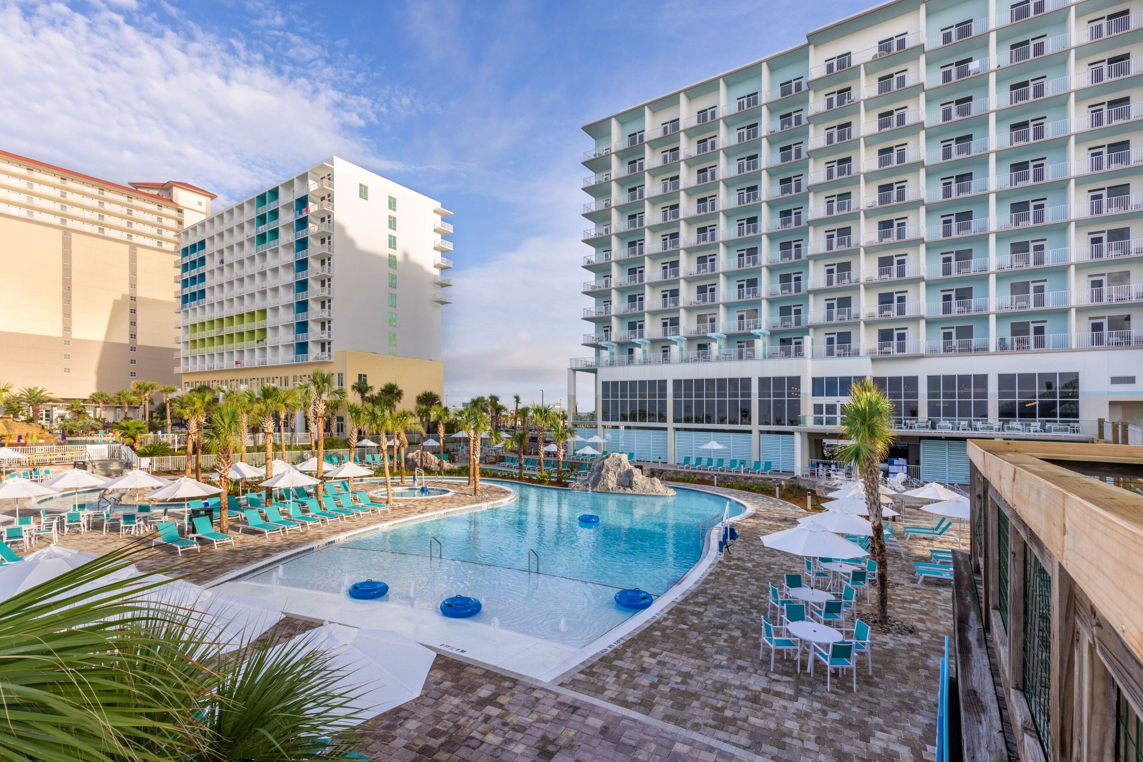 A hotel with a swimming pool, lounge chairs, and palm trees.