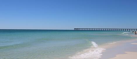 A beach with clear water and a pier extending into the ocean.