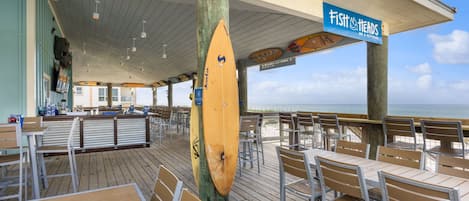 En restaurant ved stranden med udendørs siddepladser, en træterrasse og havudsigt.