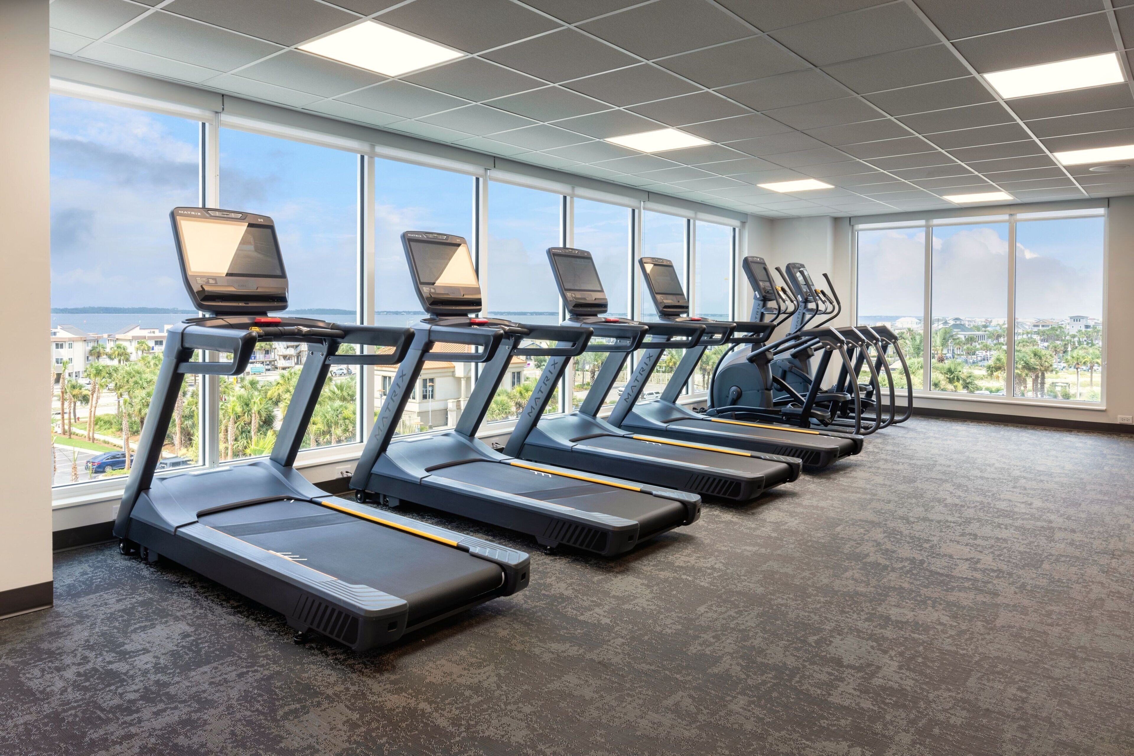 Ein Fitnessraum mit Reihe von Laufbändern, großen Fenstern und Blick auf eine Stadtlandschaft.