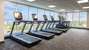 A gym with treadmills aligned in a row, large windows, and a view of a cityscape.