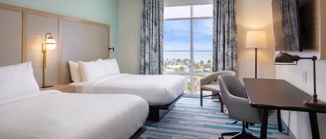 A hotel room with two beds, a desk, a chair, and a large window with curtains.