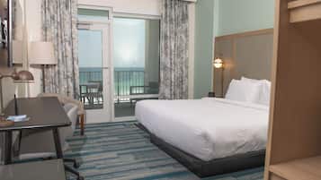 Quarto de hotel com cama, escrivaninha, cadeira, abajur e vista para a varanda.