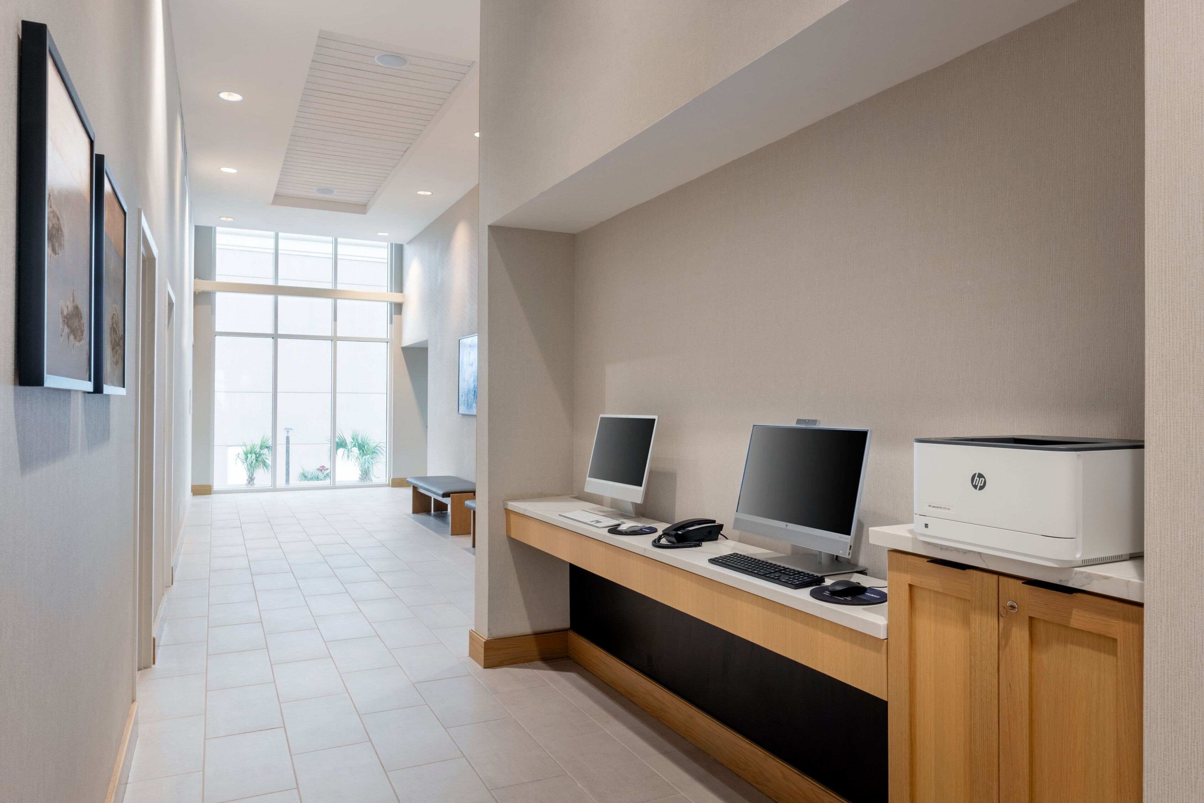 A modern office space with two desktop computers, a printer, and a bench in the background.