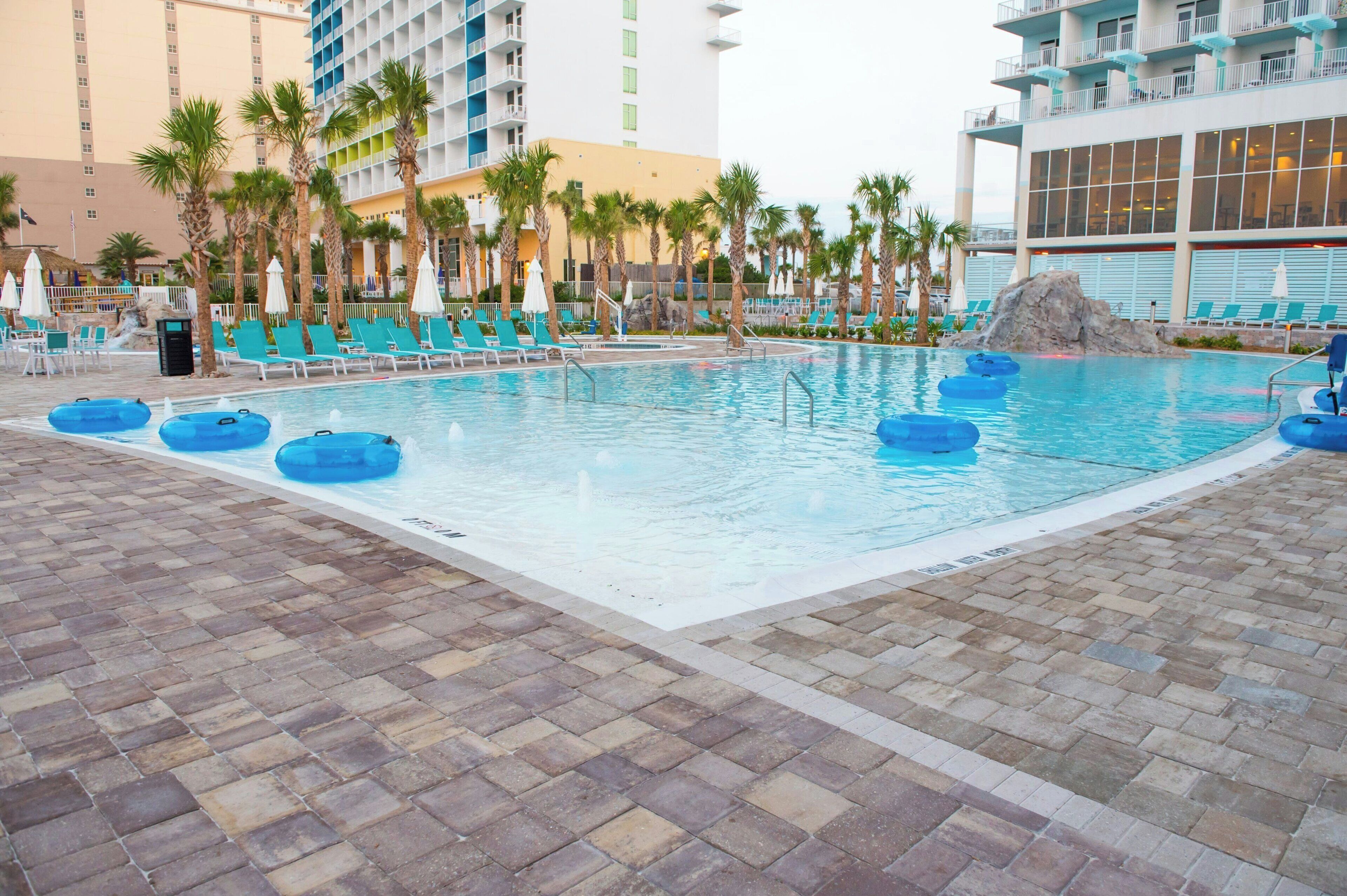 A swimming pool with lounge chairs and palm trees, surrounded by hotel buildings.