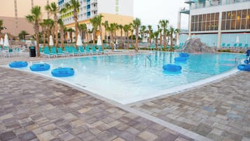 A swimming pool with lounge chairs and palm trees, surrounded by hotel buildings.