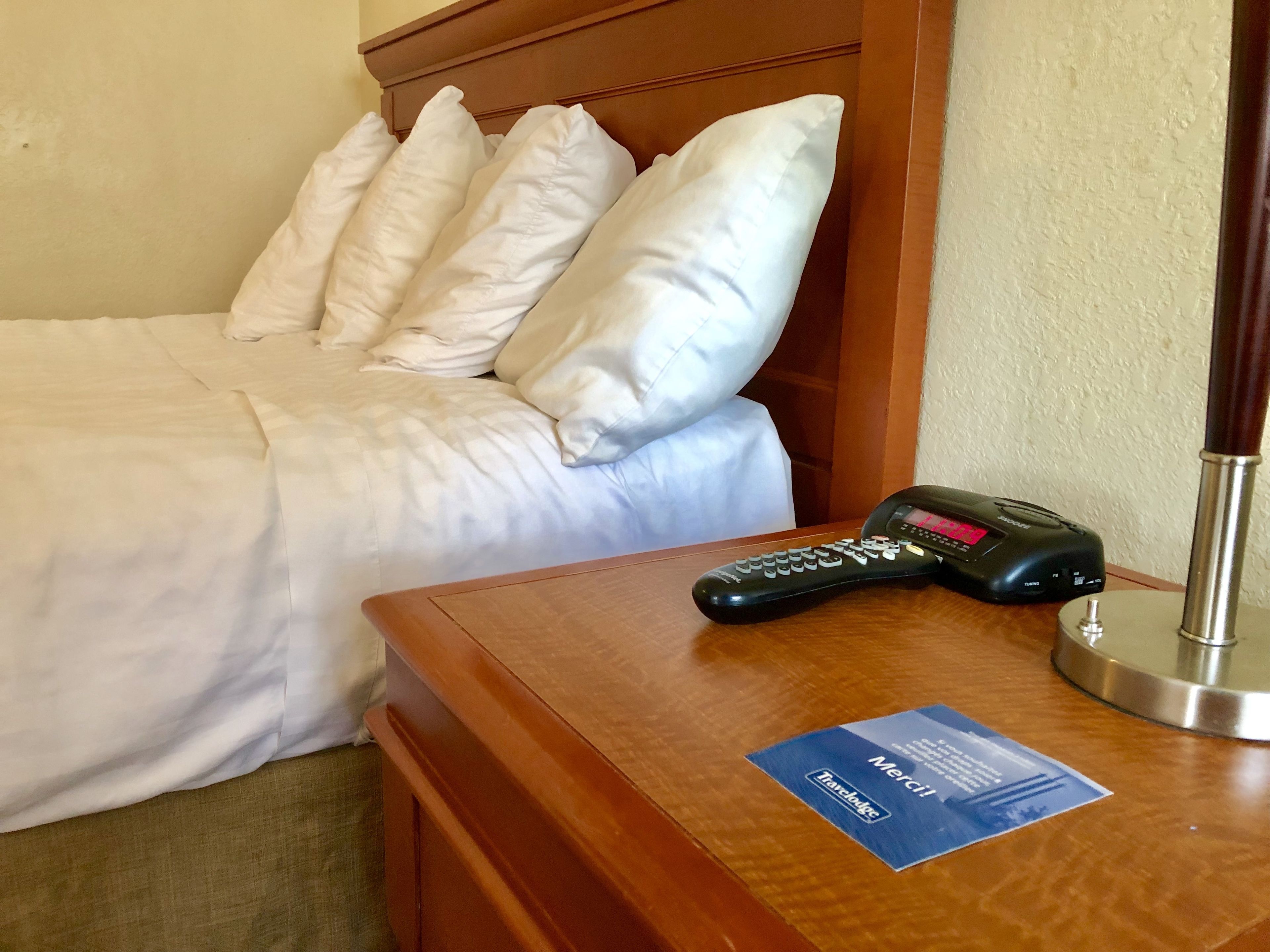 A hotel room with a neatly made bed, a bedside table with a remote control, and a card on the table.