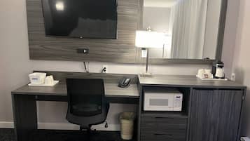 A hotel room with a wooden desk, a television, a microwave, a coffee maker, a telephone, and a trash can.