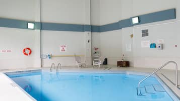 An indoor swimming pool with a diving board, chairs, and safety signs.
