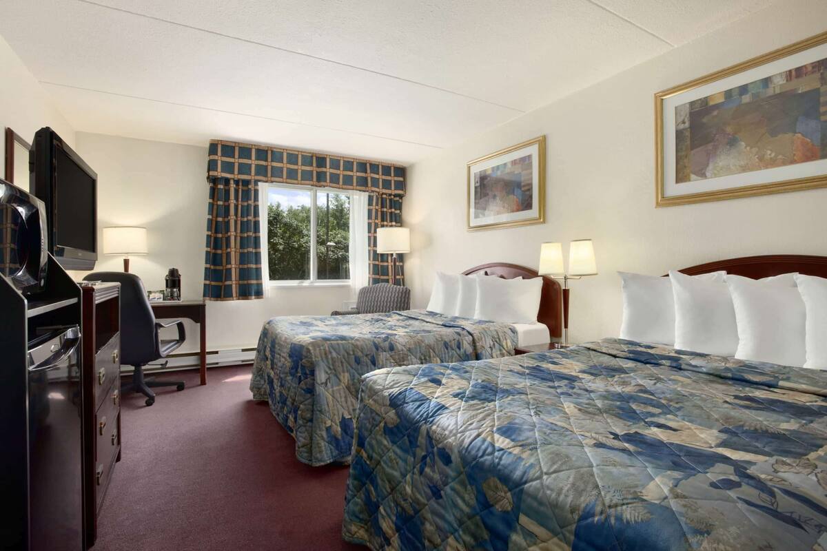 Une chambre d’hôtel avec deux lits, un bureau, une chaise, une télévision et une fenêtre donnant sur des arbres.