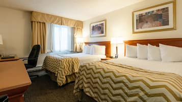 A hotel room with two beds, a desk, and a chair. There are two lamps on the nightstands and a framed picture on the wall.