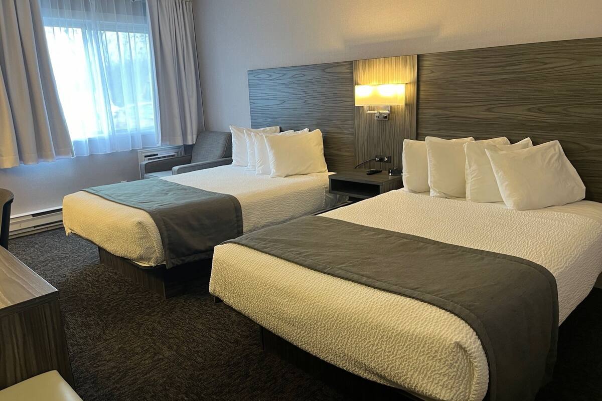 Une chambre d’hôtel avec deux lits, un bureau, une chaise, une table de chevet et une fenêtre avec des rideaux.