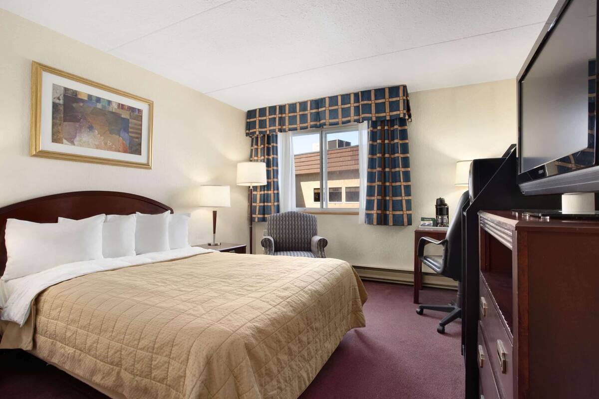 Une chambre d’hôtel avec un grand lit, un bureau avec une télévision, une chaise et une fenêtre avec des rideaux.