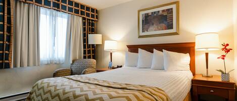 Una habitación de hotel con una cama grande, dos mesitas de noche con lámparas, una silla, una ventana con cortinas y un cuadro en la pared.