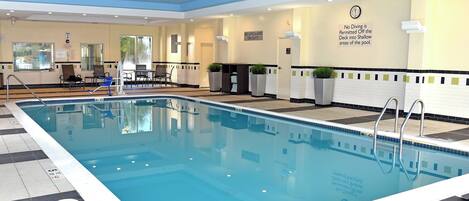 An indoor swimming pool with a lifeguard on duty sign, a clock, and a no diving sign.