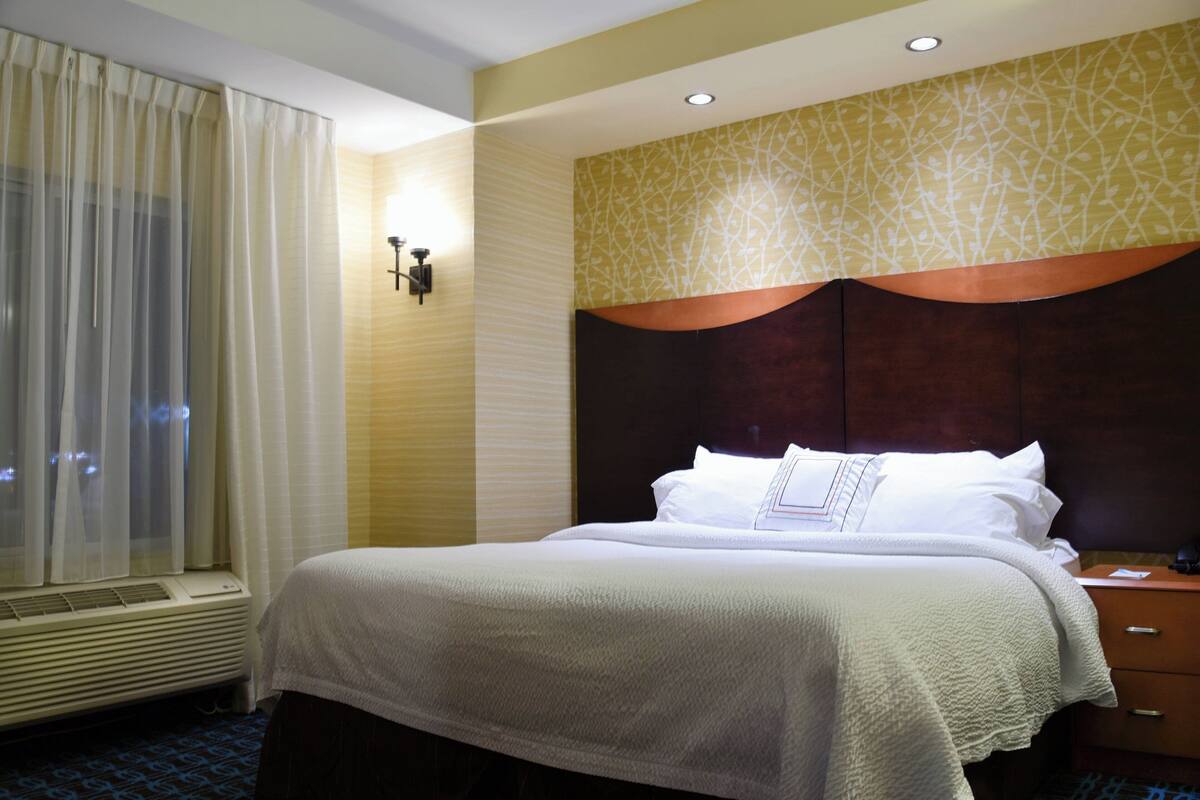 Una habitación de hotel con una cama grande, una mesita de noche, una ventana con cortinas y un muro decorado con un diseño de hojas.