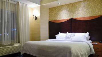 Hotelkamer met een groot bed, nachtkastje, raam met gordijnen en een muur met bladmotief.