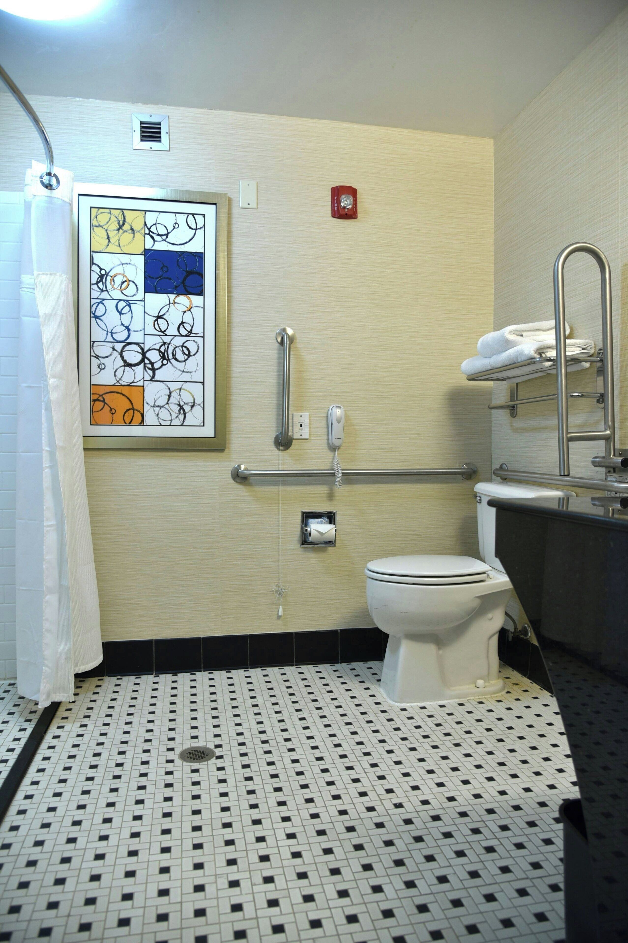 A bathroom with a white toilet, a handrail, a shower curtain, and a tiled floor.