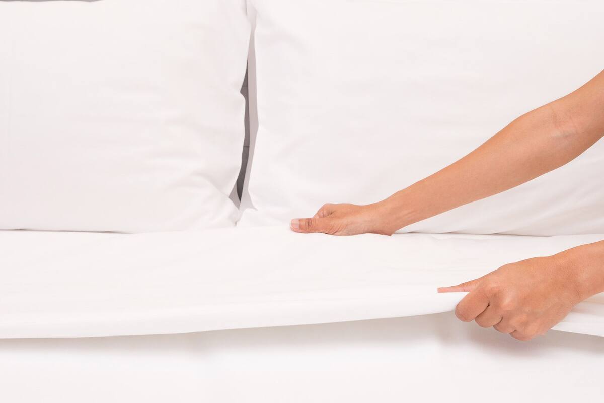 Uma pessoa ajustando um colchão branco na cama.