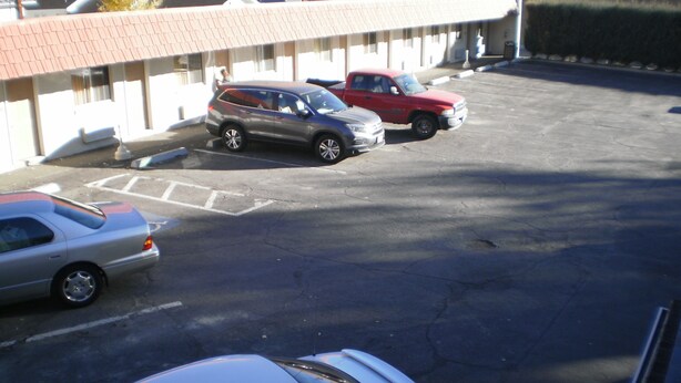 Un estacionamiento con varios autos, incluyendo un auto deportivo blanco, un SUV rojo y un sedán plateado.