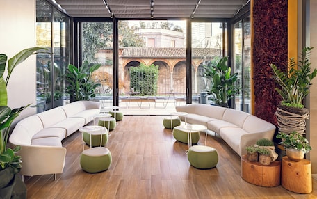 A modern lounge area with a curved white sofa, round green ottomans, and potted plants.