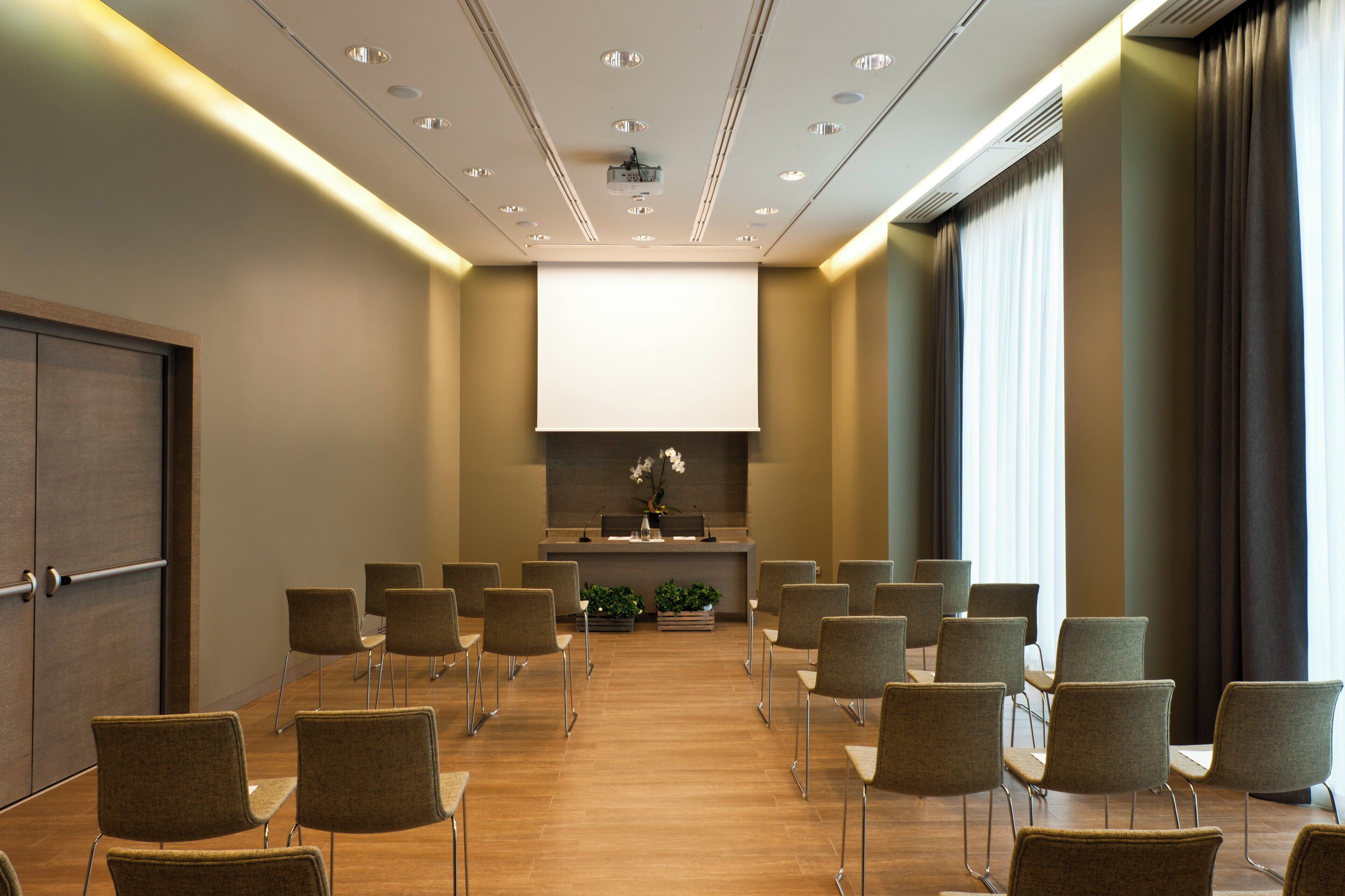 Una sala conferenze con un lungo tavolo, sedie, un podio e uno schermo per proiezioni.