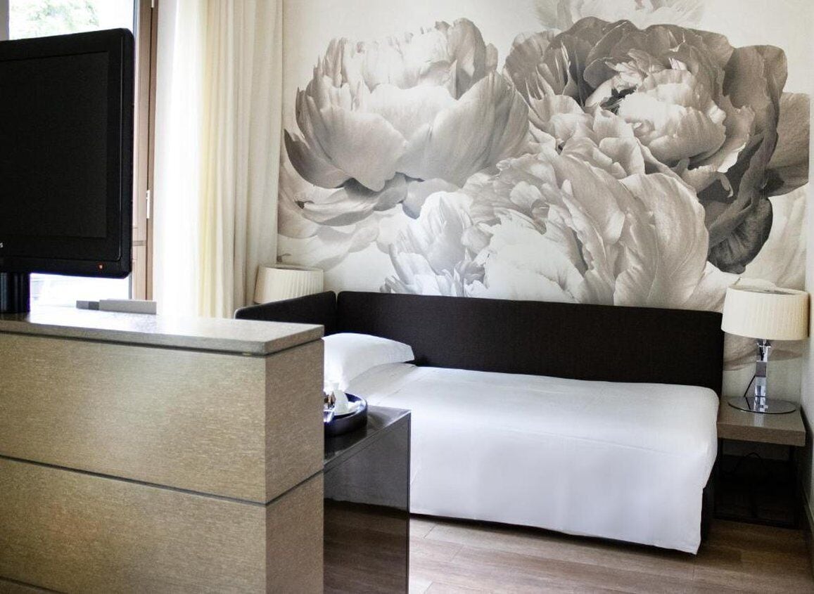 Una habitación de hotel con cama, escritorio, televisión y un cuadro grande con motivos florales en la pared.
