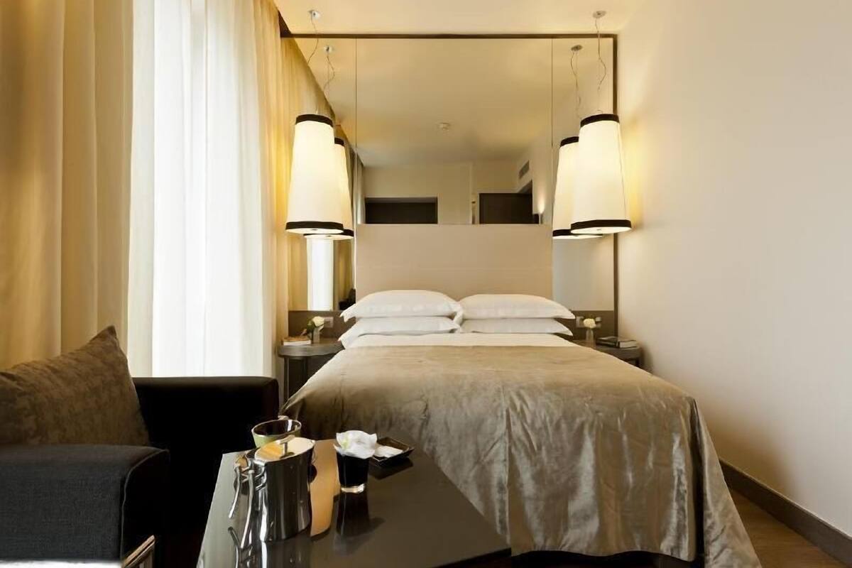 Une chambre d’hôtel avec un lit, des tables de chevet, une chaise et un grand miroir.