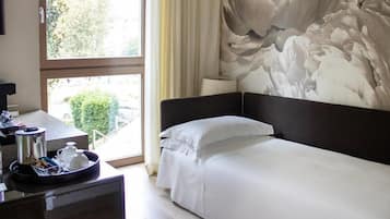 Een hotelkamer met een bed, een bureau met een dienblad ontbijtartikelen, een raam met gordijnen en een muur met een bloemmotief.