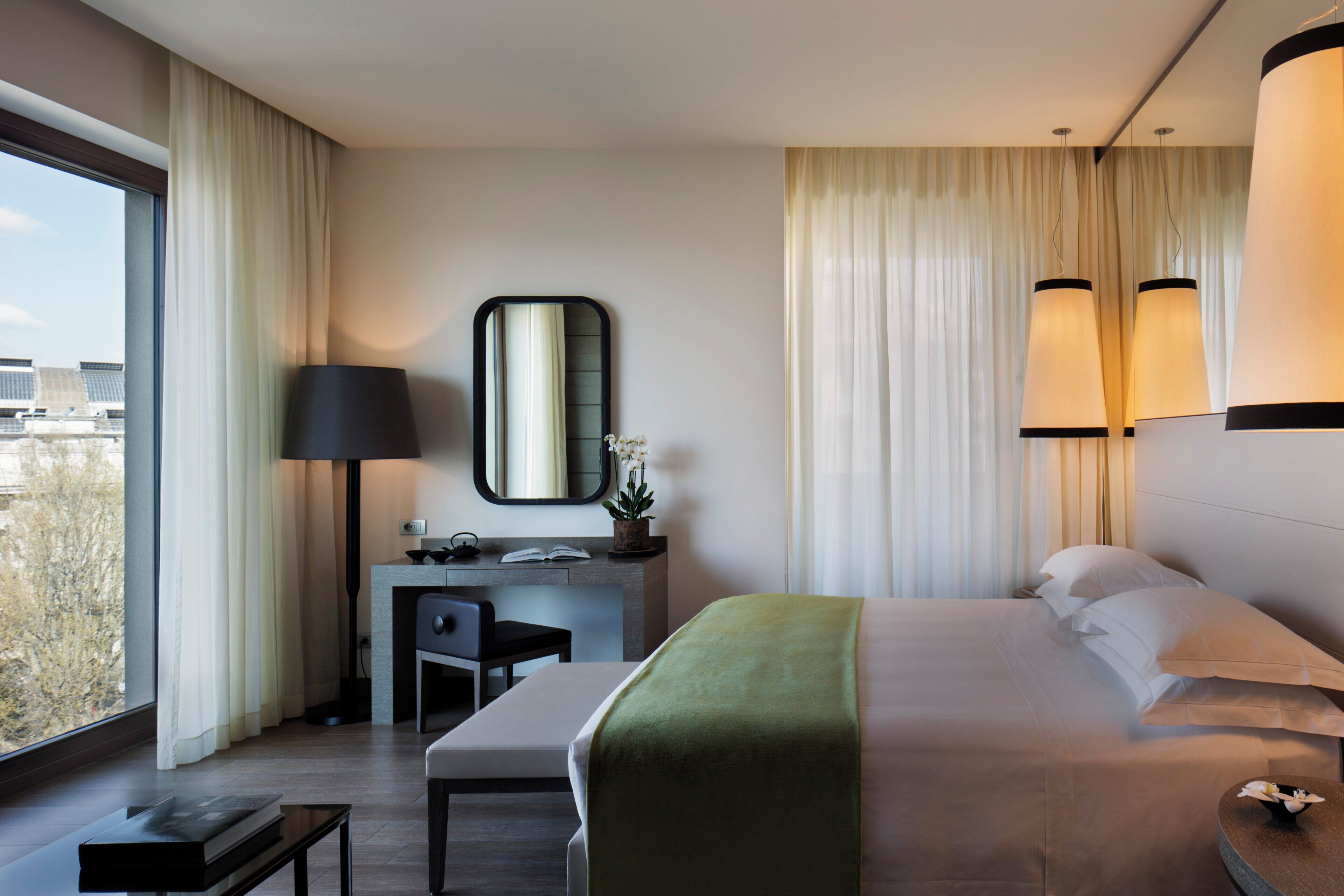 Une chambre d’hôtel moderne dotée d’un grand lit, d’un bureau avec une chaise, d’une petite table et d’une grande fenêtre donnant sur la ville.