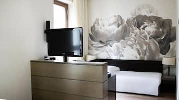 Een hotelkamer met een bed, een televisie op een dressoir, een grote bloemenmuur en een raam met gordijnen.