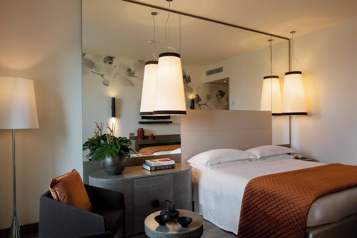 Une chambre d’hôtel moderne équipée d’un lit, d’une table de chevet, d’une lampe et d’une table basse ronde agrémentée d’objets décoratifs.