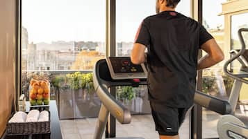 A man using a treadmill in a gym with a city view through large windows.