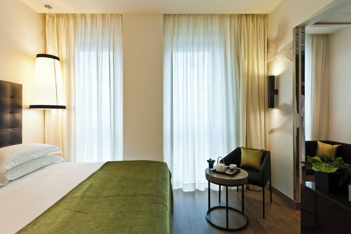 Une chambre d’hôtel avec un lit, une chaise, une petite table et un bureau agrémenté d’une plante.