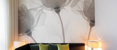 A modern living room with a dark sofa, green and yellow cushions, a small table with a vase, and two lamps on either side.