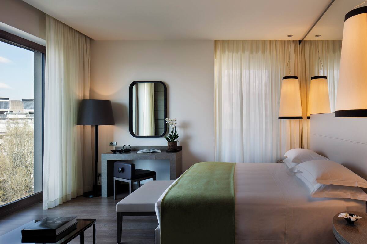 Une chambre d’hôtel moderne dotée d’un grand lit, d’un bureau avec une chaise, d’une petite table et d’une grande fenêtre donnant sur la ville.