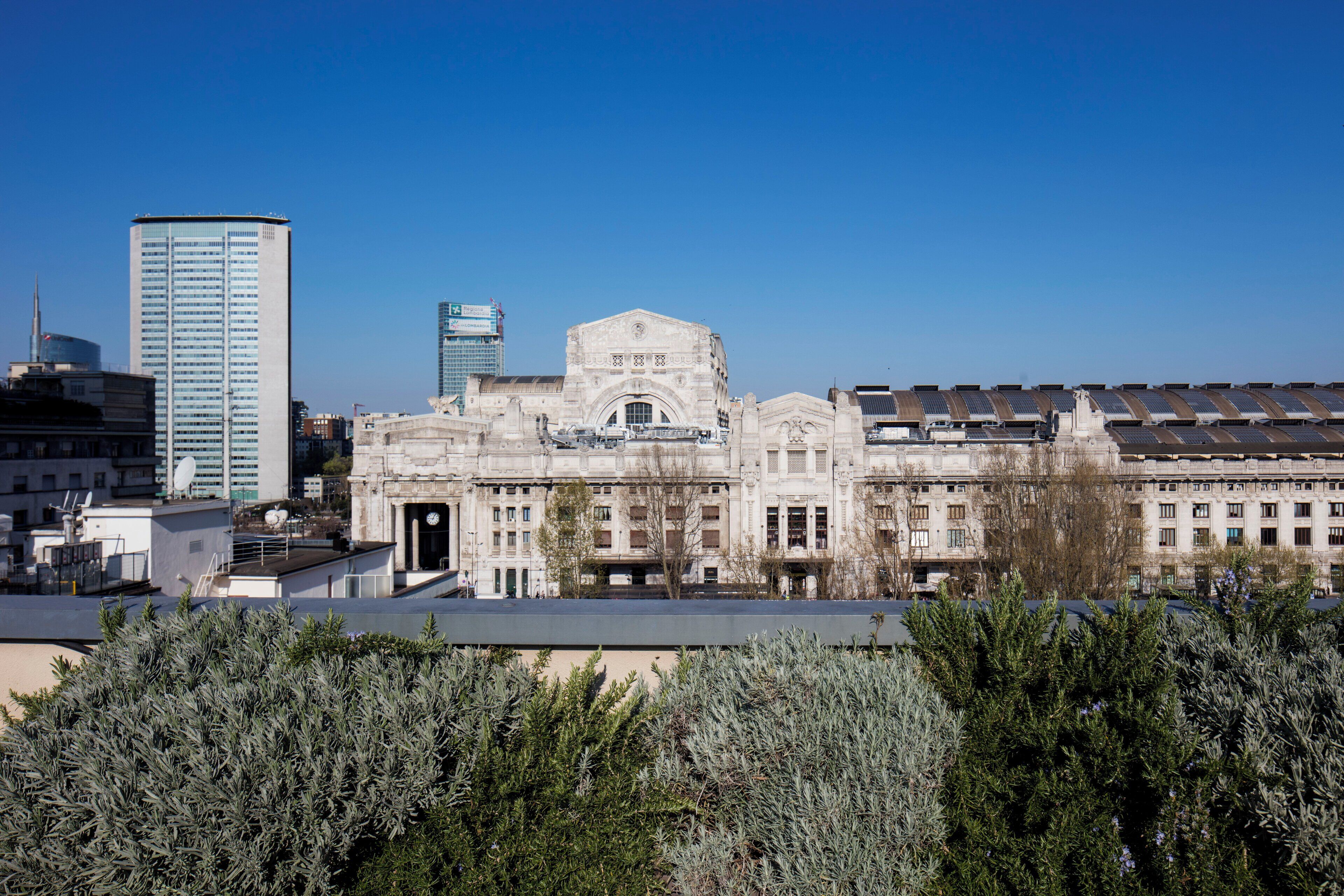 Een historisch gebouw met een centrale, gebogen entree, omringd door symmetrische vleugels, in een stedelijke omgeving met moderne wolkenkrabbers.