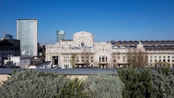 Een historisch gebouw met een centrale, gebogen entree, omringd door symmetrische vleugels, in een stedelijke omgeving met moderne wolkenkrabbers.
