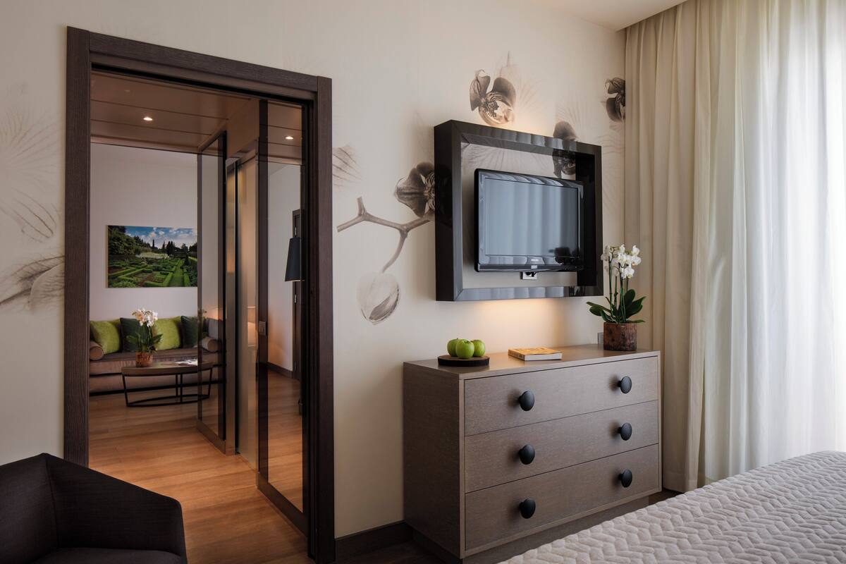 Une chambre d’hôtel comprenant un lit, une commode, un téléviseur fixé au mur et une porte donnant sur un coin salon avec un canapé et une table.