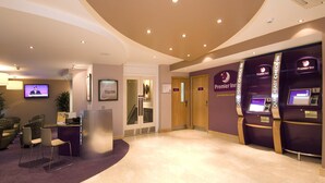 A hotel lobby with a reception desk, seating area, Premier Inn signage, and check-in kiosks. - Premier Inn London Victoria (London)