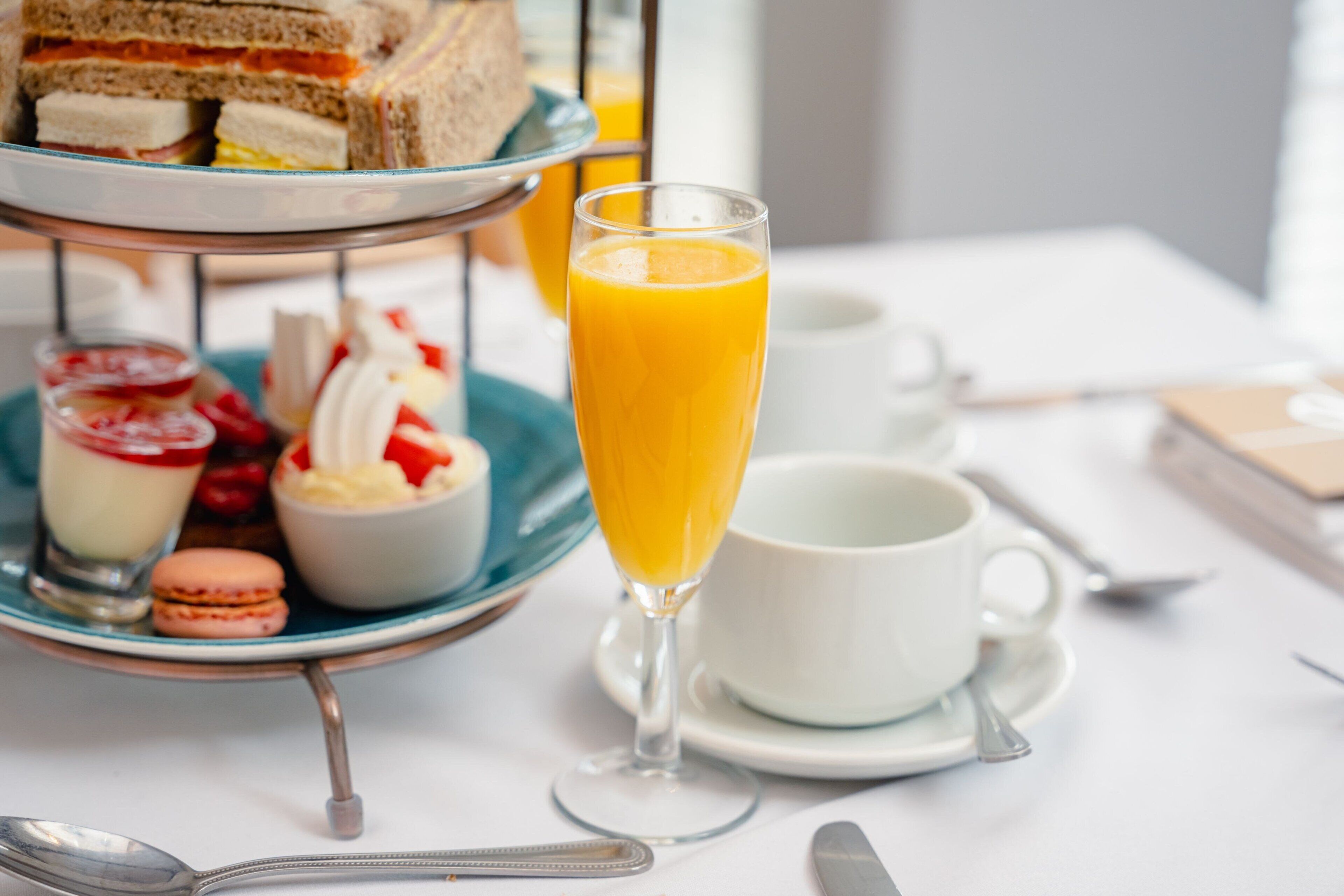 A three-tiered dessert stand with various pastries and a glass of orange juice.