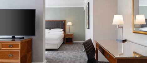 A hotel room with a bed, a desk with a chair, a television, a lamp, and a mirror.