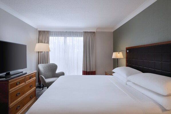 A hotel room with a bed, a TV, a chair, a dresser, and a window with curtains.